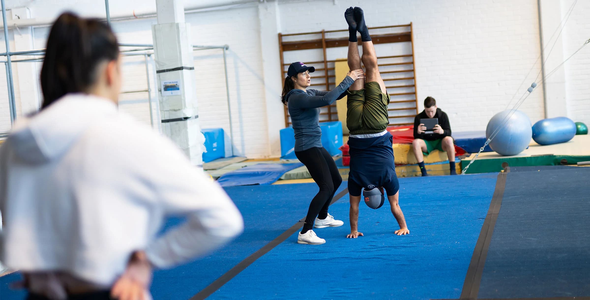 A coach spots an athlete holding a handstand in a gym while a classmate watches, at Otago Polytechnic's Institute of Sport, Exercise and Health